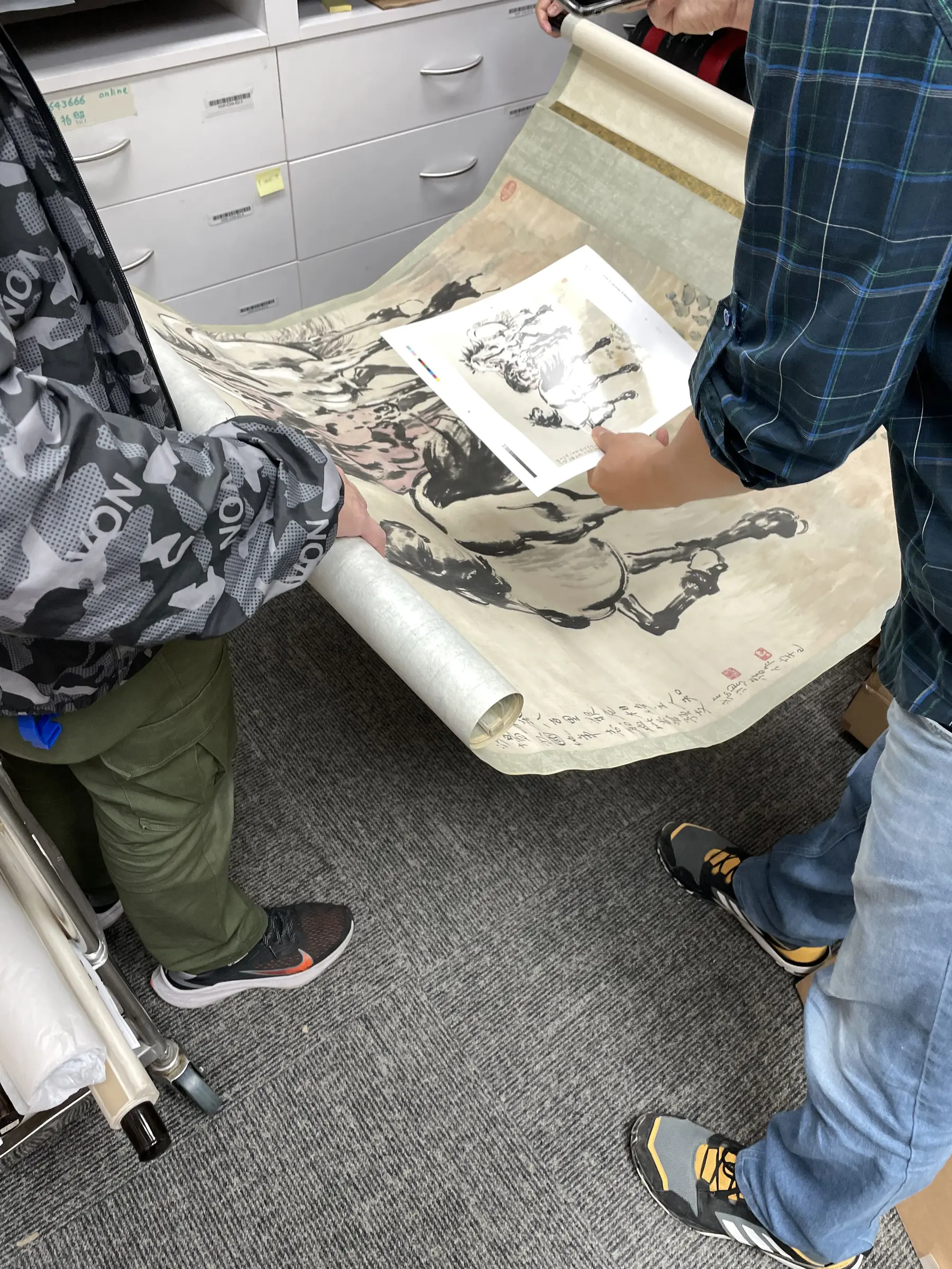 Team members reviewing a long proof beside the artwork.